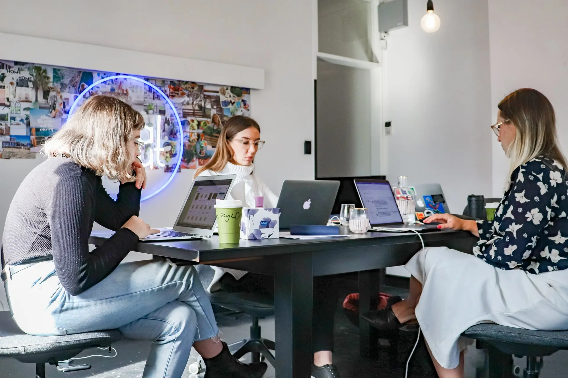 3 women at a large table doing content marketing on their laptops