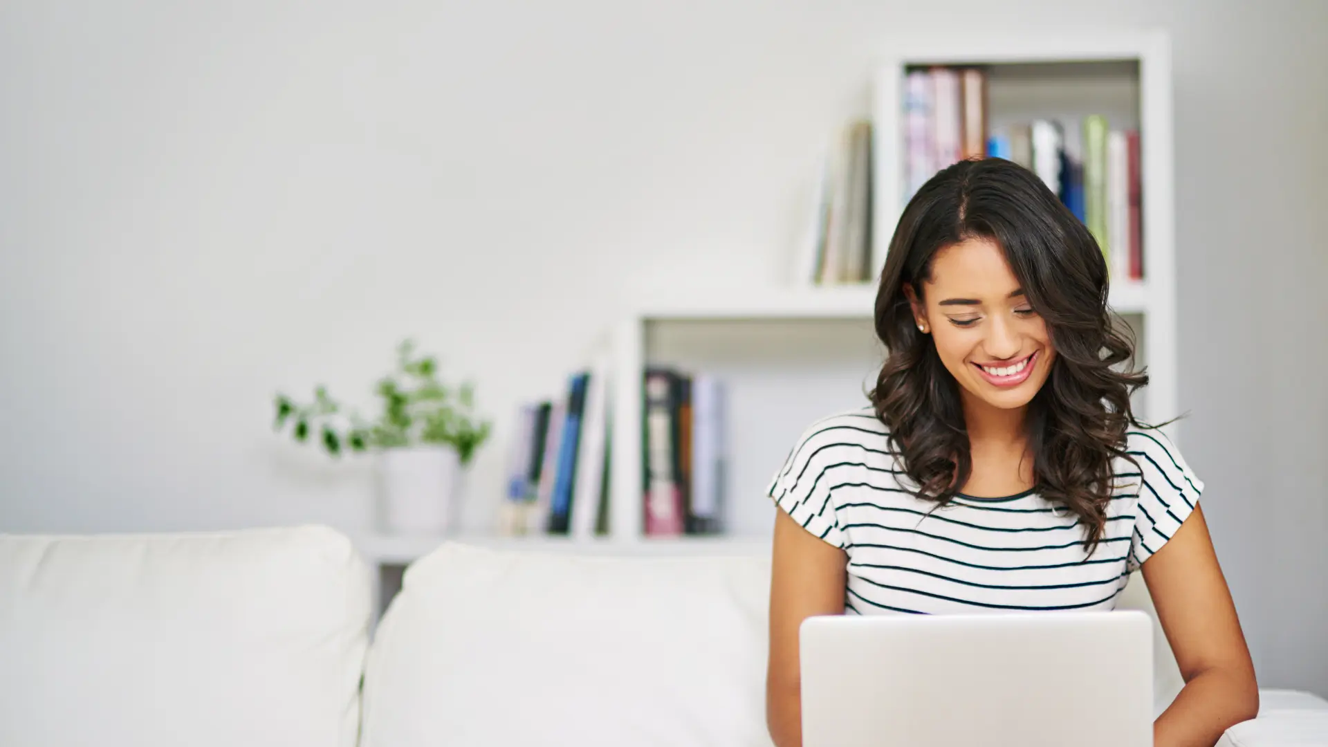 Woman sitting on a white sofa doing content marketing on her laptop