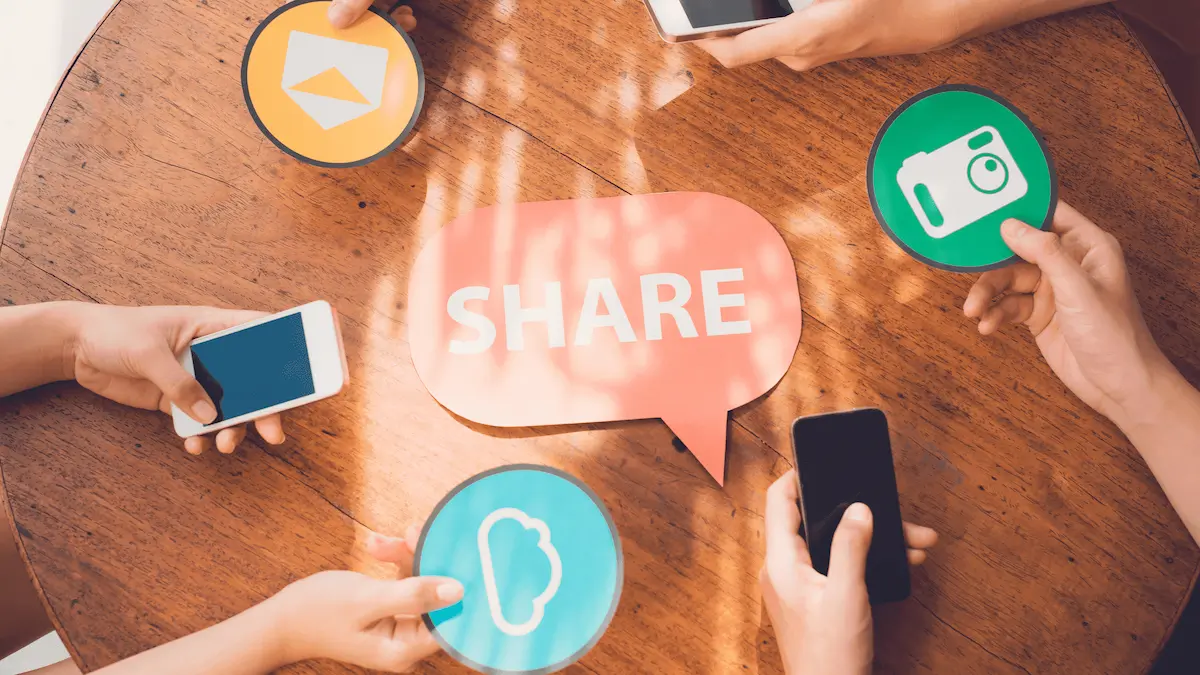 A pink speech bubble cutout on a table with the word 'SHARE' on it in white letters. This is surrounded by shareable content examples, like phones, emails, icloud.