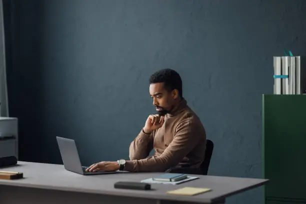 An office scene showing a professional at his desk, using a laptop for various business activities and strategies.