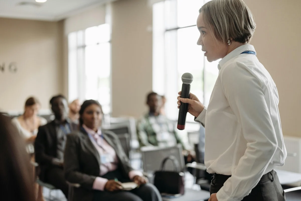 A female speaking into a microphone giving a presenation in front of a few people