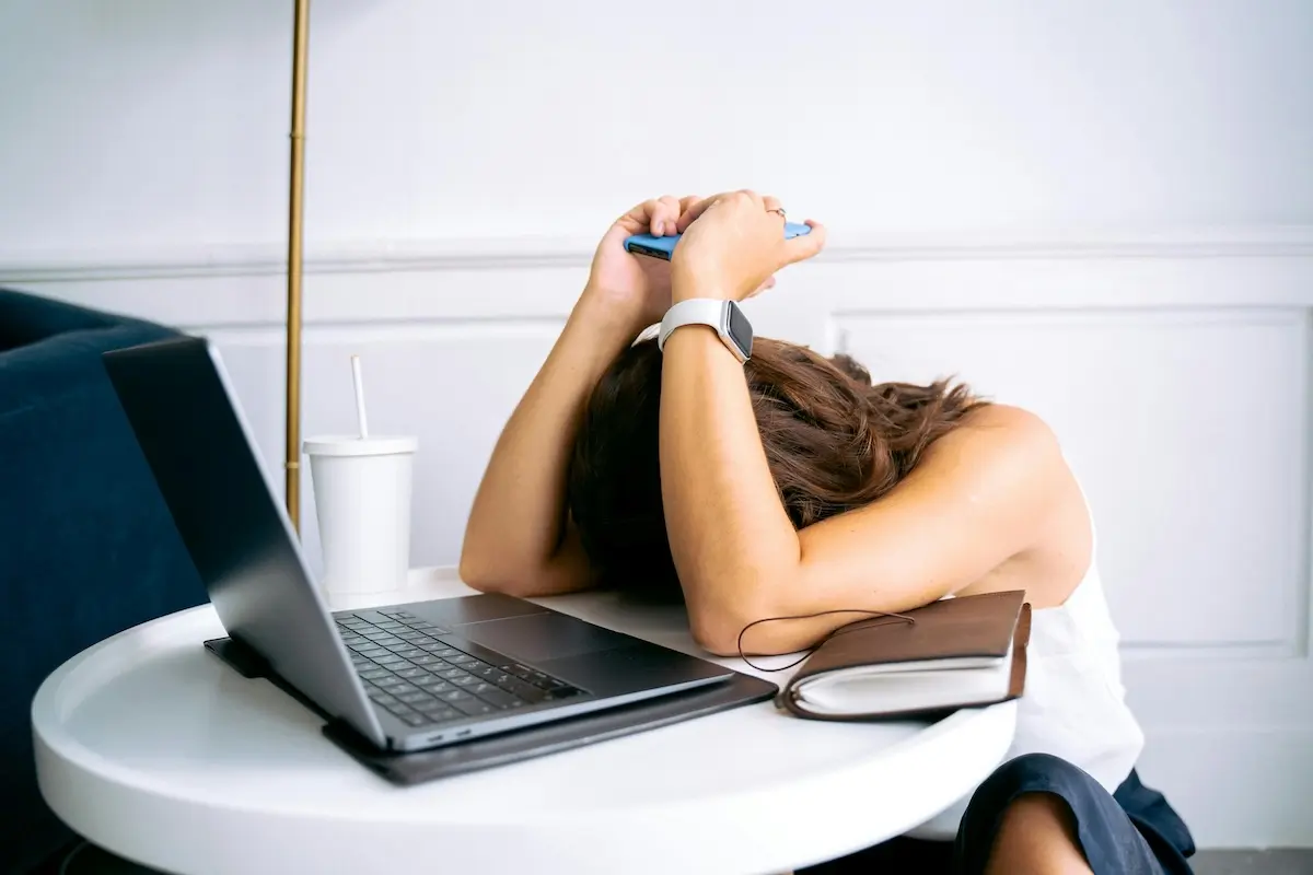 Stressed woman with her forehead on the table between her arms, laptop in front of her