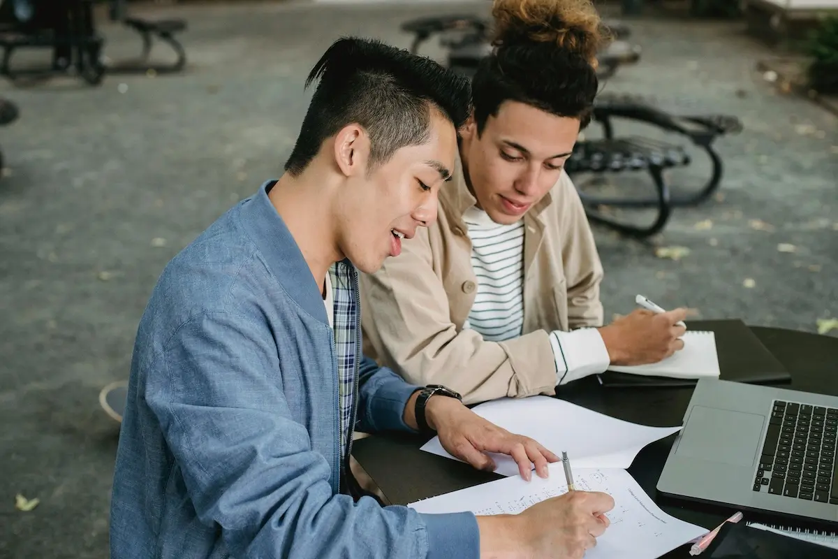 Two young male friends writing notes on an outside table