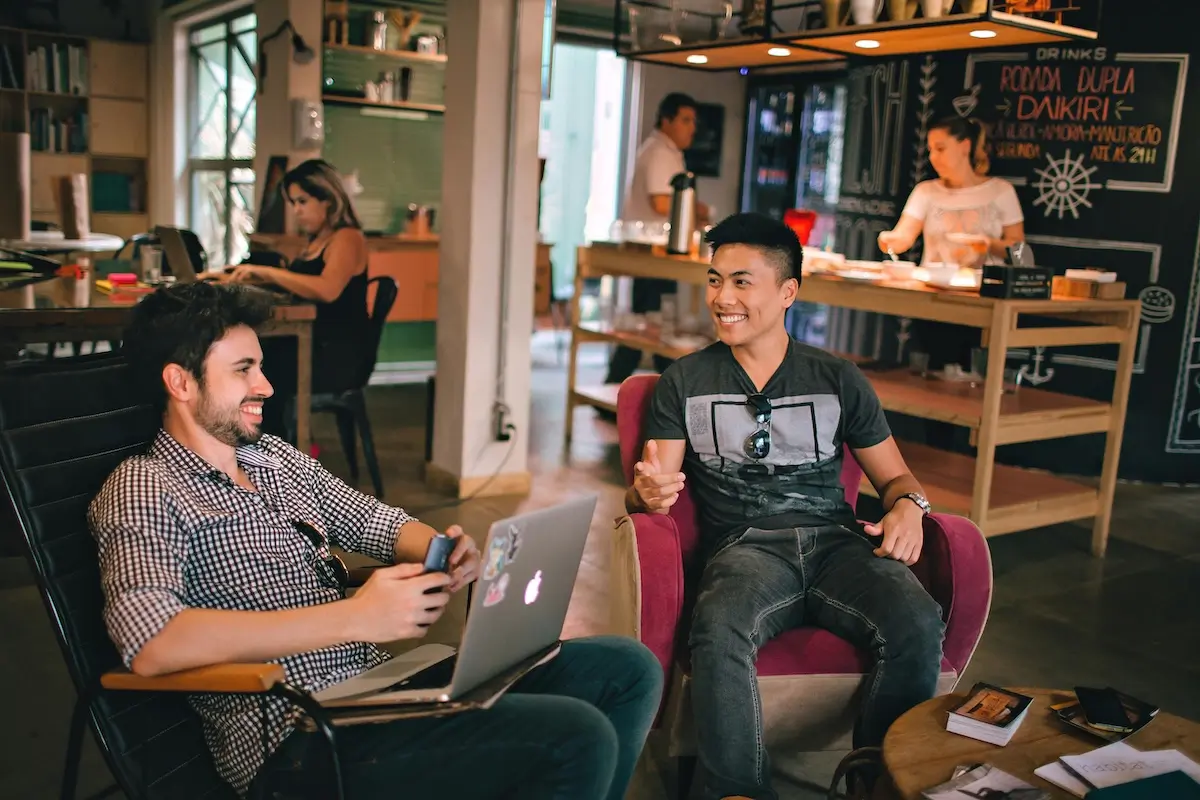 Two young men sitting in a cafe. One has a AirMac on his lap