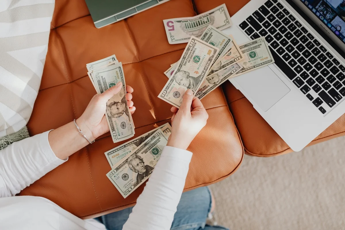 Woman with lots of dollar bills by her laptop