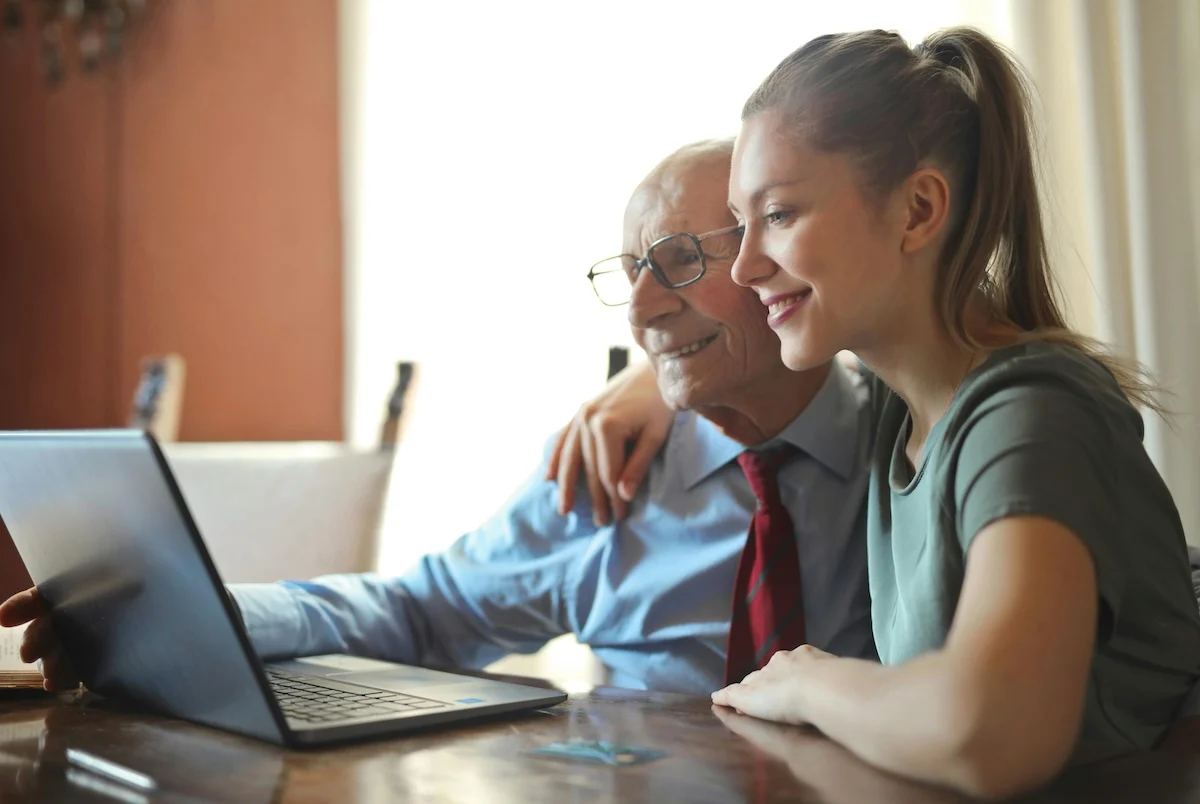Young woman with her arm over the shoulder of an old man, looking at a laptop