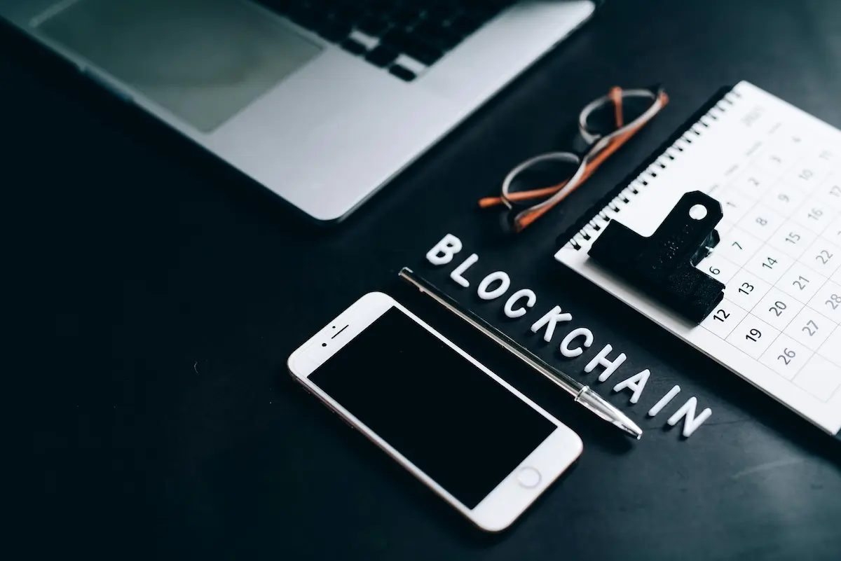 Blockchain on a black desk next to a pen, phone, and laptop by Leeloo the first on Pexels. com