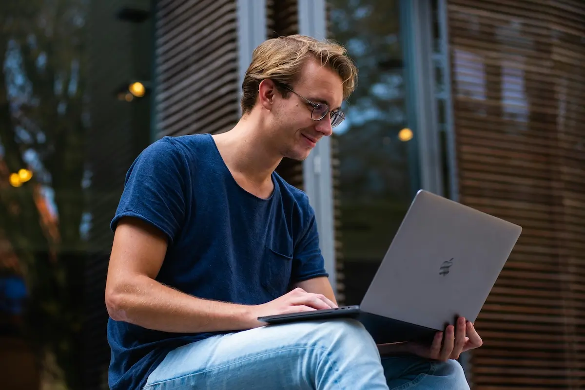 A man sitting outside on his MacBook by Marta Klement on Pexels. com