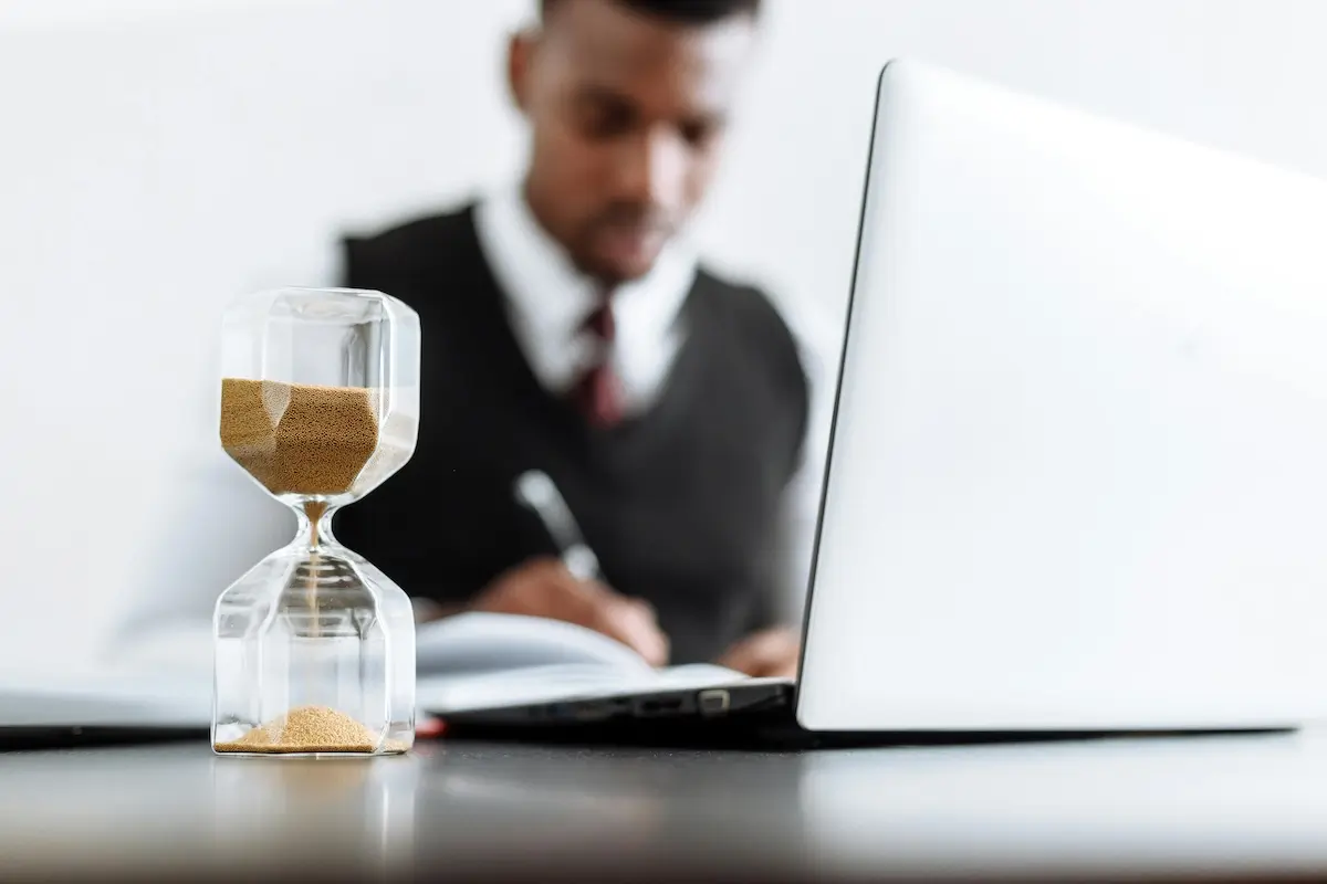 A man writing copy in front of a laptop and hourglass by Thirdman on Pexels. com