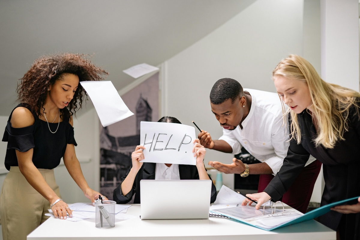 Overworked people in an office, not optimisied for AI, one holds up the word 'HELP' on a piece of paper by Yan Krukau on Pexels. com