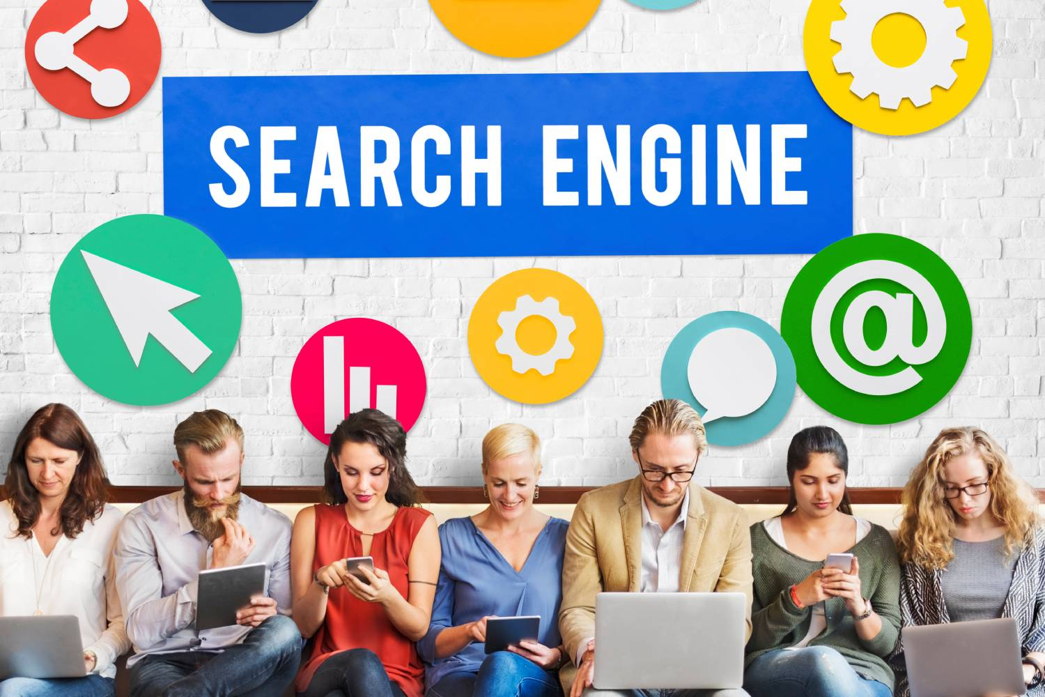 A line of people sitting using their tech goods. Search Engine is on the wall behind them