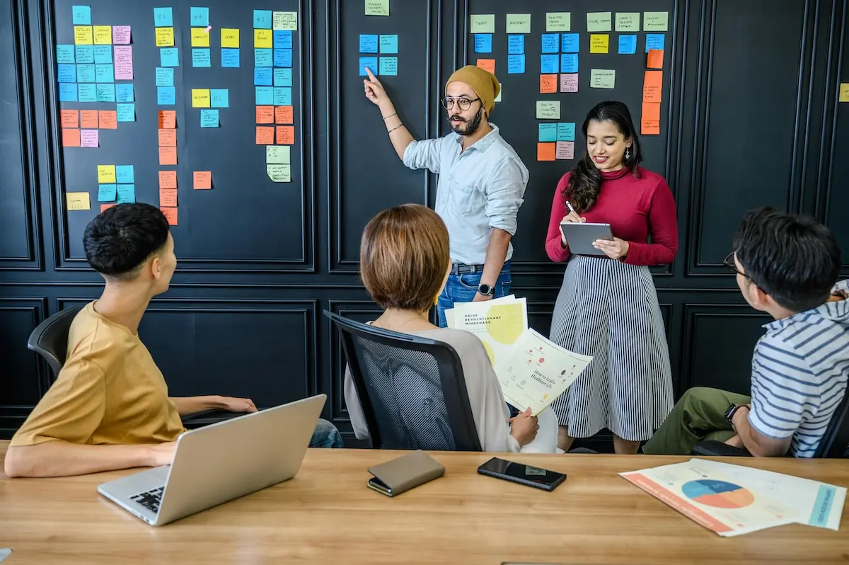 A man pointing at a postage note stuck to the wall in a business meeting by Ketut Subiyanto on pexels.com