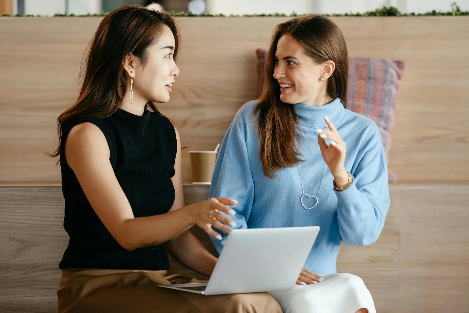 Two sitting women chatting at work, one has a laptop on her lap by Alexander Suhorucov on Pexels