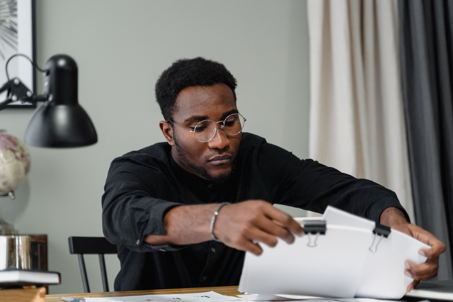 Bespectaculed black man looking at clipped white A4 sheets by Tima Miroshnichenko on Pexels