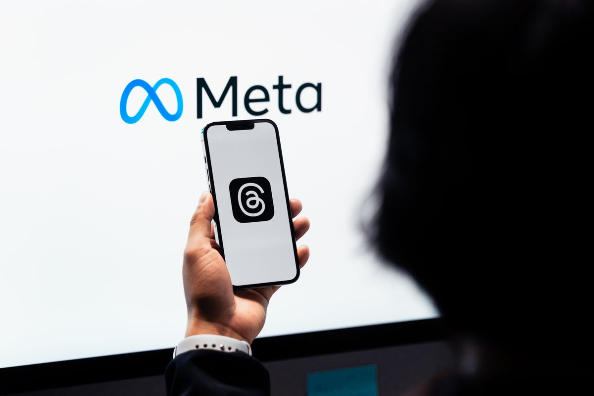 Image of Hands holding smartphone with Meta Threads logo on screen, Meta branding in background by Julio Lopez 
