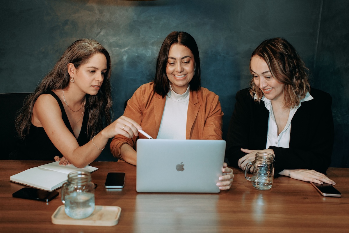 Three woman looking at internal linking content hubs on one laptop, with smiles on their faces by Helena Lopes on Pexels